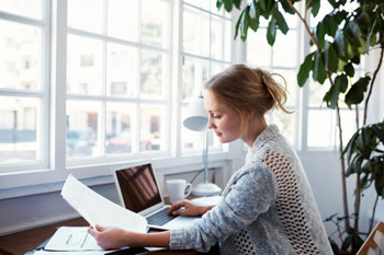 Eine Fernstudentin für Sozialmanagement sitzt zur Hause am Schreibtisch und lernt am Laptop
