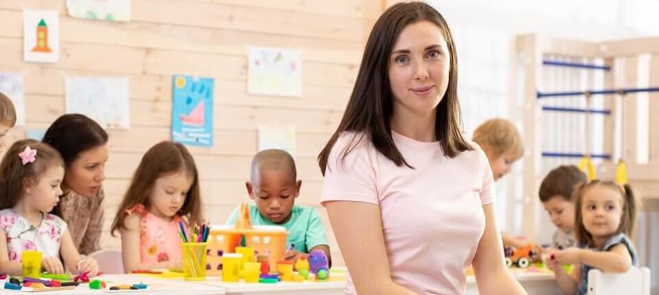 Stundentin kuemmert sich um Kleinkinder die im Hintergrund spielen