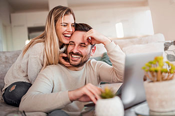 Paar sitzt im Wohnzimmer vor Laptop im Fernstudium